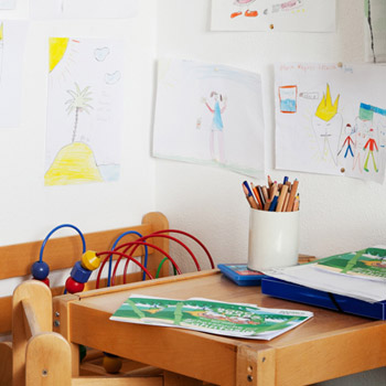 Kinderspielecke mit kleinem Tisch und Stühlen, Spielsachen und gemalten Bildern an der Wand